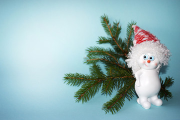 Smile snowman with Christmas tree branch on a light blue background with copy space. Christmas and New Year concept, minimalism. Invitation.
