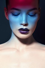 Bright contrasting beauty makeup portrait of a woman in blue and red shadow tones. Perfect clean skin and face makeup, dark lipstick on plump lips