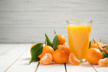 Glass of fresh tangerine juice and fruits on white wooden table