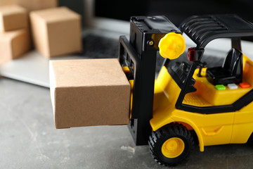 Toy forklift with box near laptop on table. Logistics and wholesale concept