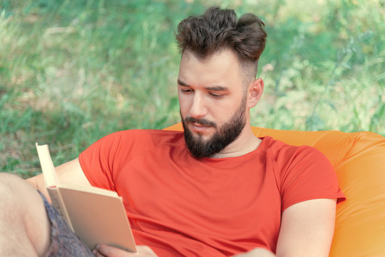 A Man With A Beard Reading A Book In Nature. Concept Of Summer Recreation And Education