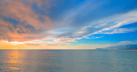 Sunset over the sea and mountains, cloudy sky 
