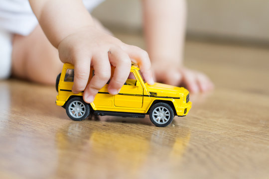 A child plays with a baby typewriter on a brown wooden floor in natural light. the boy is holding a yellow toy car. the concept of children's development and leisure. children's room.