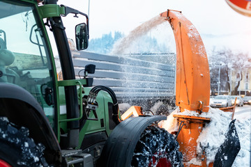 Big tractor with chains on wheel blowing snow from city street into dump truck body with...
