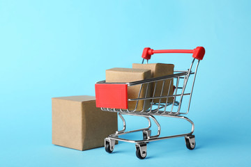 Shopping cart and boxes on light blue background. Logistics and wholesale concept