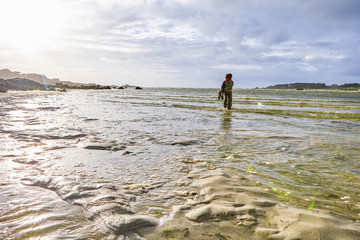 Active children in rainwear standing in the low water of the sea at a beach, beautiful light reflections