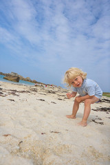 Suspiciously looking cute little boy in the sand of a beach, playing with the sand, summer holiday