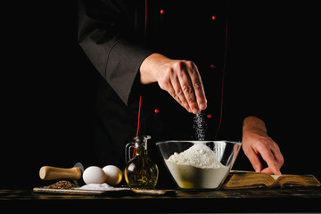 Dough preparation process. Chef adds ingredients to flour on a black background.