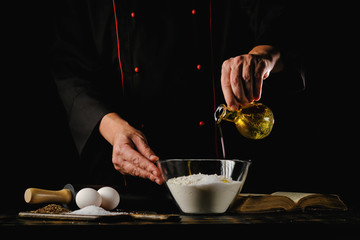 Dough preparation process. Chef adds ingredients to flour on a black background.
