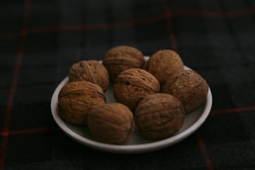 Inshell walnuts on a plate against a dark background.