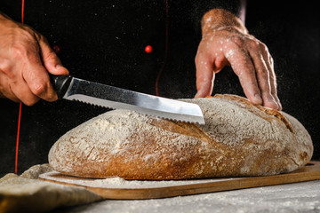 Whole grain bread put on kitchen wood plate with a chef holding  knife for cut. Fresh bread on table close-up. Fresh bread on the kitchen table The healthy eating and traditional bakery concept