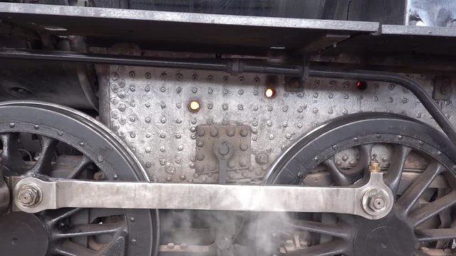 Close up of steam locomotive train wheels with steam visible and fire seen in the boiler through two ventilation holes
