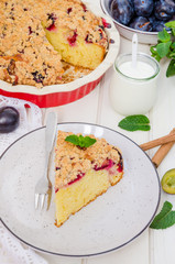 Pie with plums and shtreisel on a plate on a white wooden background. Rustic style. Homemade baking.