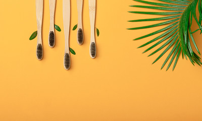 Five bamboo, wooden toothbrushes with black bristles are located with green leaves on a yellow background. Eco friendly concept, zero waste, recycling, eco. Flat lay with copy space