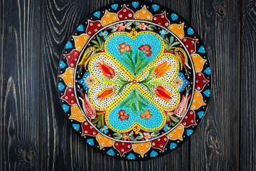 Ukrainian Petrykivka decorative plate, traditional decorative painting style, handicraft souvenirs on dark wooden background