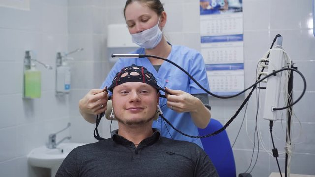 Preparing for EEG brain test at doctor's office. Installing device for electroencephalography examination of young man.