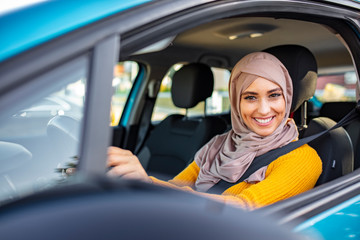 Young attractive smiling arab woman in traditional wear trying out new car. Portrait of muslim...