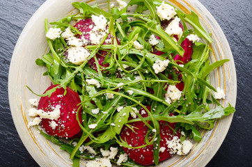Top view at clay dish with beetroot arugula and feta cheese salad on slate stone tray closeup view