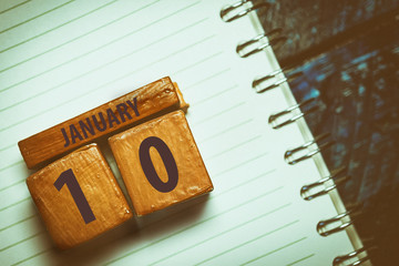 january 10th. Day 10 of month,Handmade wood cube with date month and day placed on a lined notebook on a blue background. artistic coloring.  winter month, day of the year concept