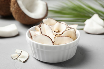 Tasty coconut chips in bowl on grey table
