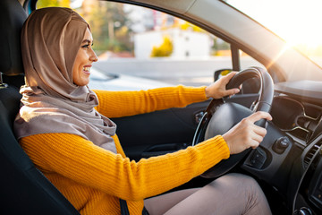Beautiful young happy smiling Muslim woman driving her new car at sunset. Young Muslim woman on...
