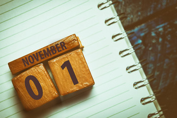 november 1st. Day 1 of month, Handmade wood cube with date month and day placed on a lined notebook on a blue background. artistic coloring.  autumn month, day of the year concept