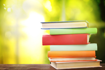 Stack of colorful books on wooden table against blurred green background. Space for text