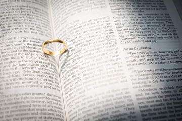 gold wedding ring with shadow heart on open Holy Bible in sepia with crackle overlay