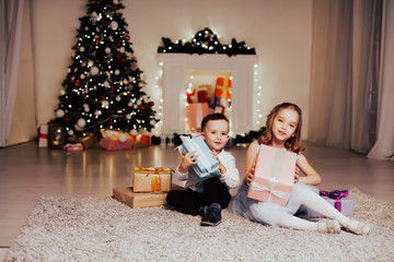 Obraz na płótnie Canvas boy and girl family opens Christmas gift new year holiday lights Christmas tree garlands