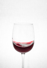 A glass of red wine and a small splash, waves of wine inside the glass on a white background