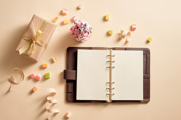 Empty notebook with gift boxes and a cupcake with a candies on light yellow background, top view