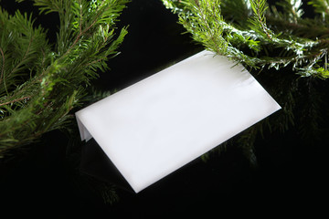 White envelope without inscriptions on a black background with fir branches. Copy space. The view...