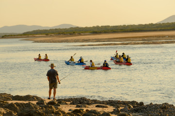 A group of people kayaking  passing a man fishing at Seventeen Seventy in Queensland, Australia.