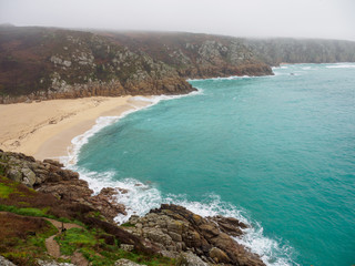 Wide aerial view of a sandy bay beach along the coastal granite cliffs of Porthcurno. Conrwall, United Kingdom. Travel and tourism. - 310677360