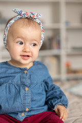 Cute baby girl with hairband (ribbon), smilling. Adorable child at home.