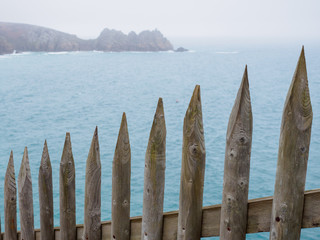 Wide closeup of a sloped wooden picket fence along the coastal cliffs of Porthcurno beach on a foggy day. Cornwall, United Kingdom. Travel and nature. - 310677513