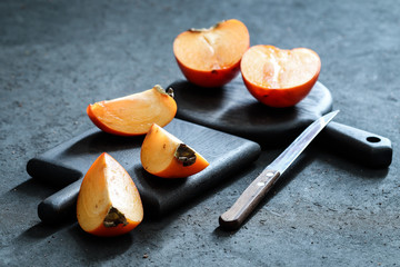 Still life with fruit, whole and chopped persimmon, knife and decorative Board on a dark background
