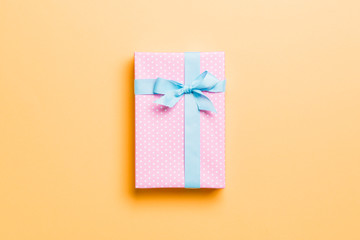 wrapped Christmas or other holiday handmade present in paper with blue ribbon on orange background. Present box, decoration of gift on colored table, top view with copy space