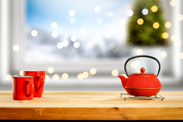 Kettle brower on wooden table and free space for your product. Blurred window sill background with chrsitmas tree and lights.Landscape of mountains and winter time.Copy space and sun light. 