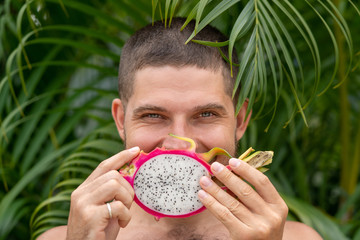 Close-up portrait man holding dragon fruit pitahaya in his hands against his face and smiling. Useful properties of fruits.