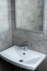 Ceramic washbasin with mirror in modern washroom with grey tile