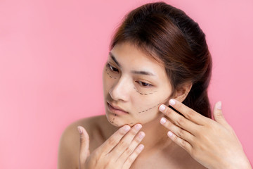Obraz na płótnie Canvas Surgeon drawing marks on woman face against pink background. Plastic surgery concept
