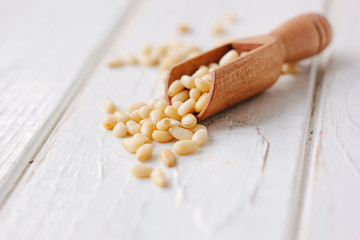 Cedar or pine nuts in a wooden scoop over white table.