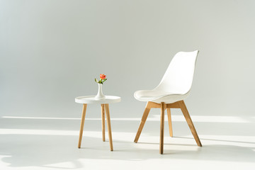 White trendy chair by table with rose in vase on grey background