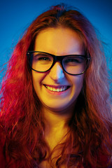 Fototapeta premium Caucasian woman's portrait isolated on blue studio background in neon light. Beautiful female model with red hair in casual style. Concept of human emotions, facial expression, sales, ad. Laughting.