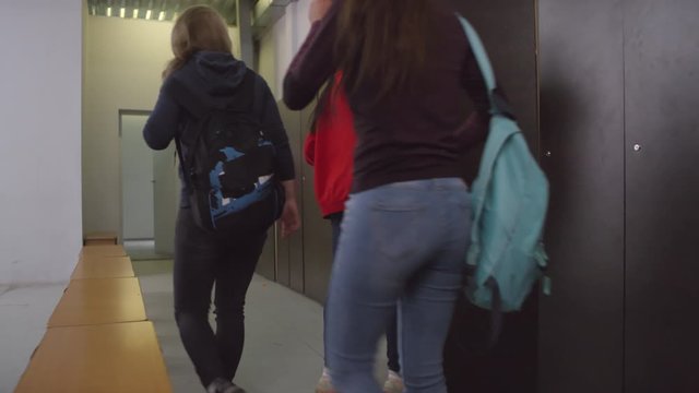 Sequence of shots of young female soccer athletes walking into locker room, changing their clothes, talking and using smartphone while preparing for game