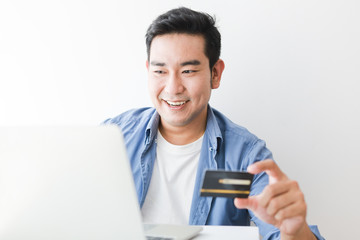 Asian handsome man in blue shirt using credit card with laptop computer shopping online