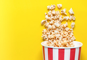 Paper cup with spread popcorn on color Popcorn viewed from above on yellow background.