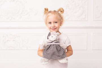 Little blond cheerful girl holds toy bear in hands and smile