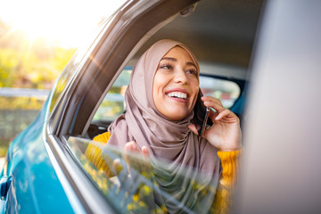 Young muslim business woman sitting in car. Muslim girl with scarf on her head sitting in the car and talking on the phone. Muslim business woman in car.